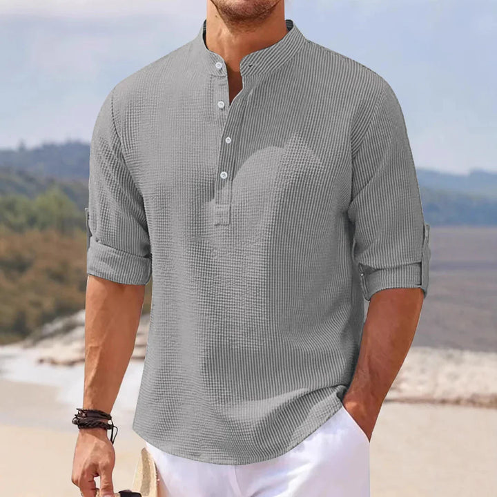 Man wearing casual grey textured henley shirt with rolled-up sleeves on a beach background