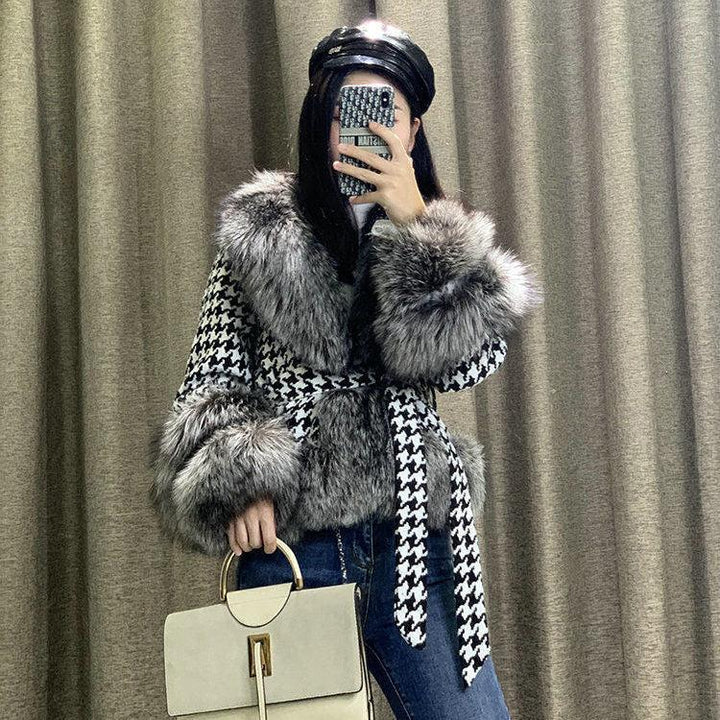 Woman in black and white houndstooth coat with fur trim, black leather cap, holding beige handbag