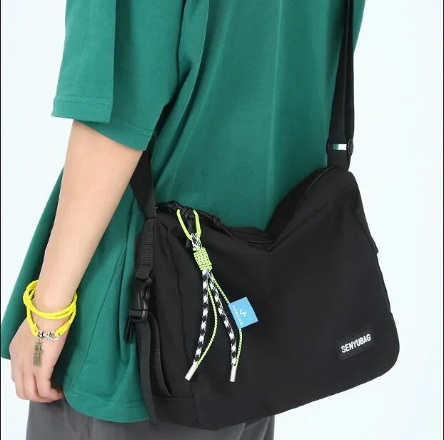 Person wearing a green shirt carrying a black SENYUBAG shoulder bag with rope accents