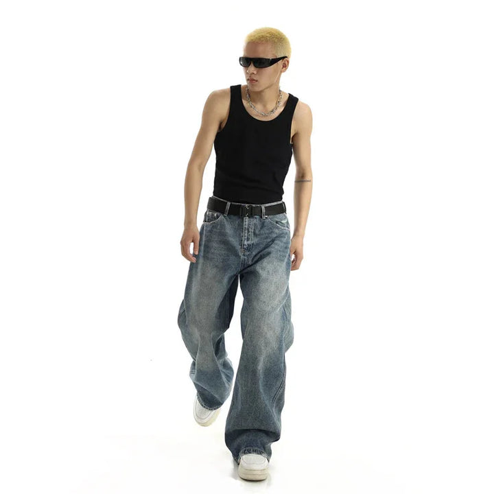 Man with blonde hair wearing black tank top, baggy blue jeans, white sneakers, and black sunglasses