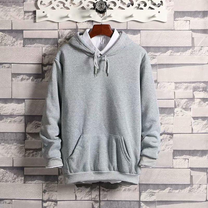 Light gray hooded sweatshirt with front pocket and drawstrings displayed on wooden hanger against gray brick wall