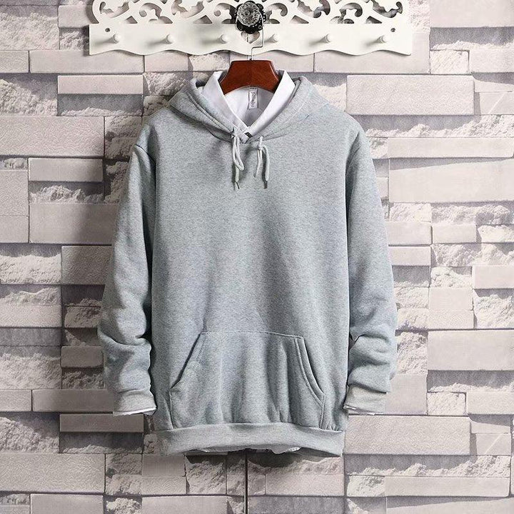 Light gray hooded sweatshirt with front pocket and drawstrings displayed on wooden hanger against gray brick wall