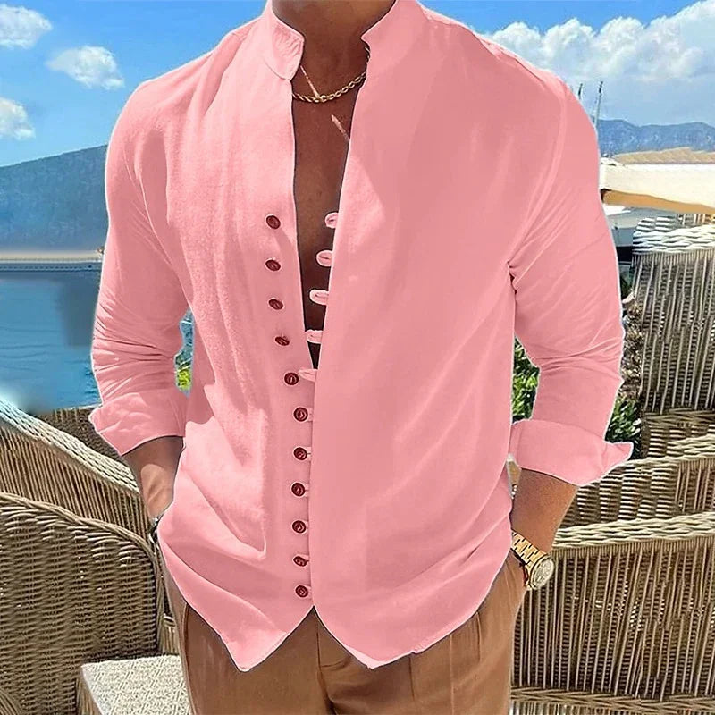 Man wearing pink Mandarin collar shirt with brown buttons and rolled-up sleeves outdoors by wicker chairs