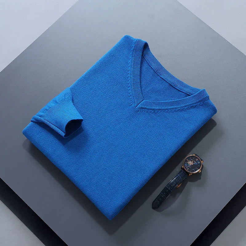 Neatly folded blue V-neck sweater with a dark wristwatch on gray surface
