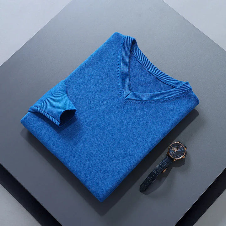 Neatly folded blue V-neck sweater with a dark wristwatch on gray surface
