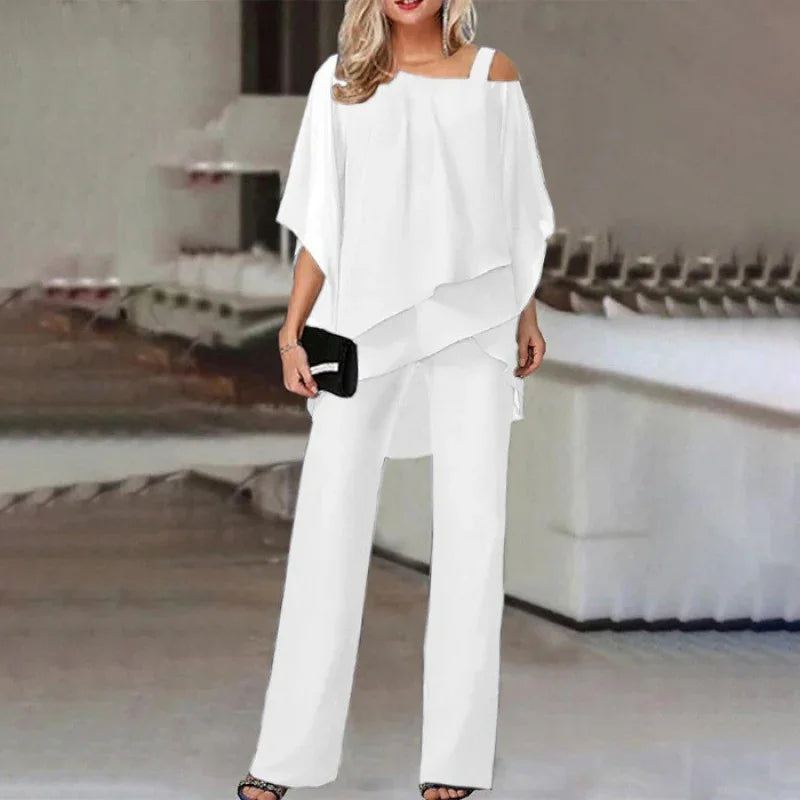 Woman wearing white asymmetrical top with shoulder straps and matching wide-leg pants holding black clutch