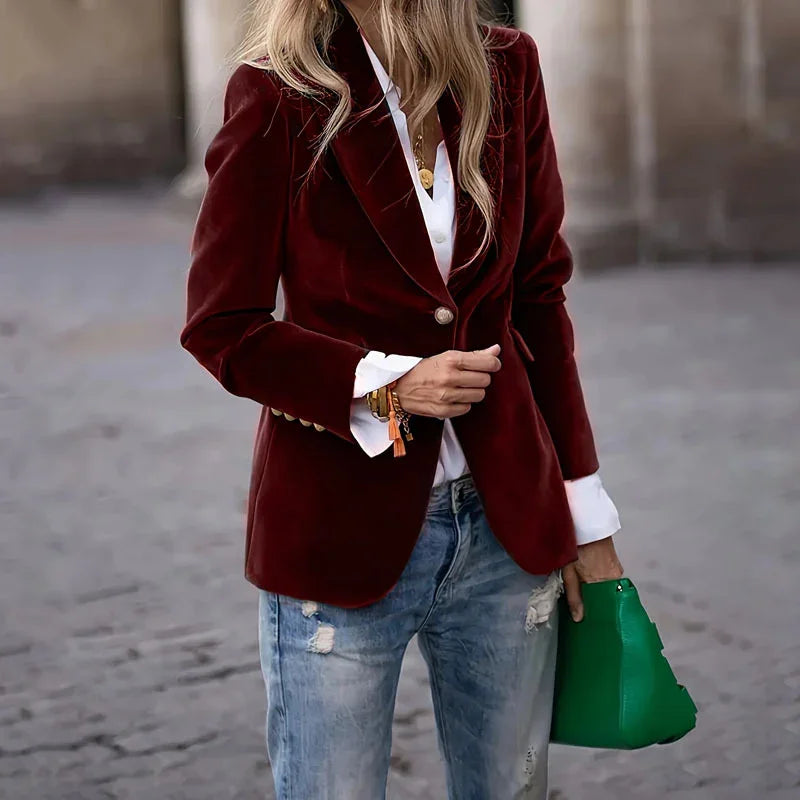 Woman wearing burgundy velvet blazer, white shirt, distressed jeans, and holding green handbag