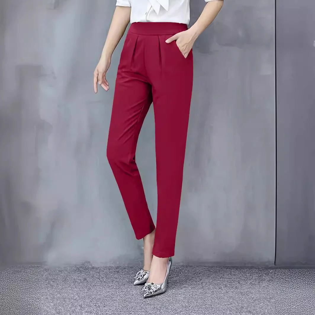 Woman wearing slim fit red formal trousers and silver high heels against gray wall