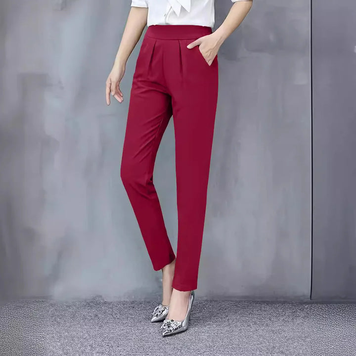 Woman wearing slim fit red formal trousers and silver high heels against gray wall