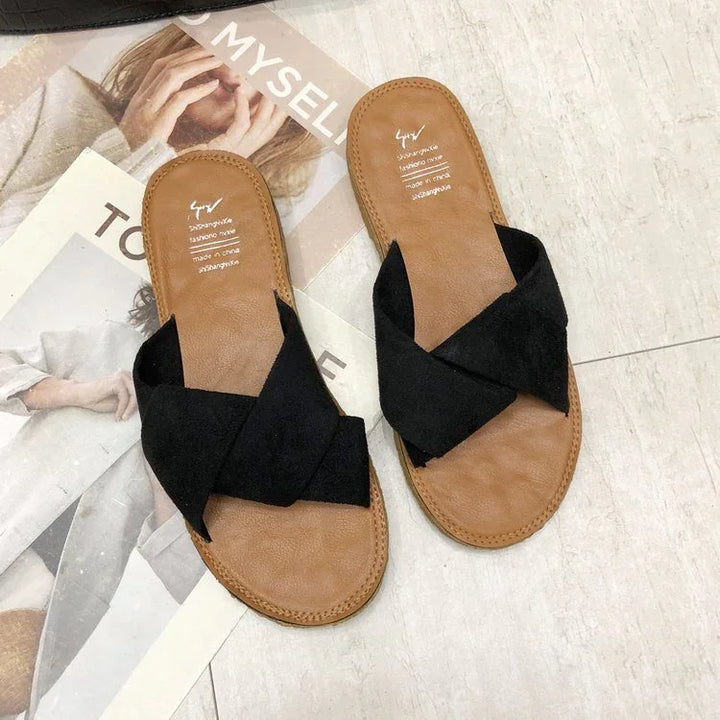 Pair of brown sandals with black crisscross straps on tiled floor with magazine background