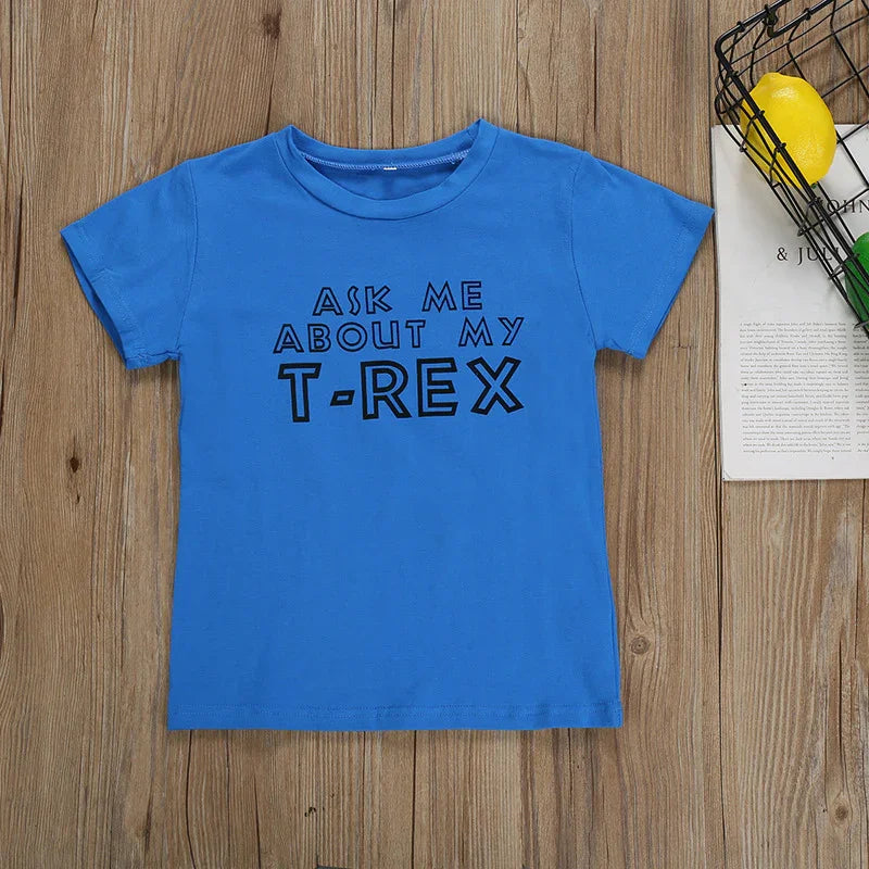 Blue children's t-shirt on wooden background with black text 'ASK ME ABOUT MY T-REX'