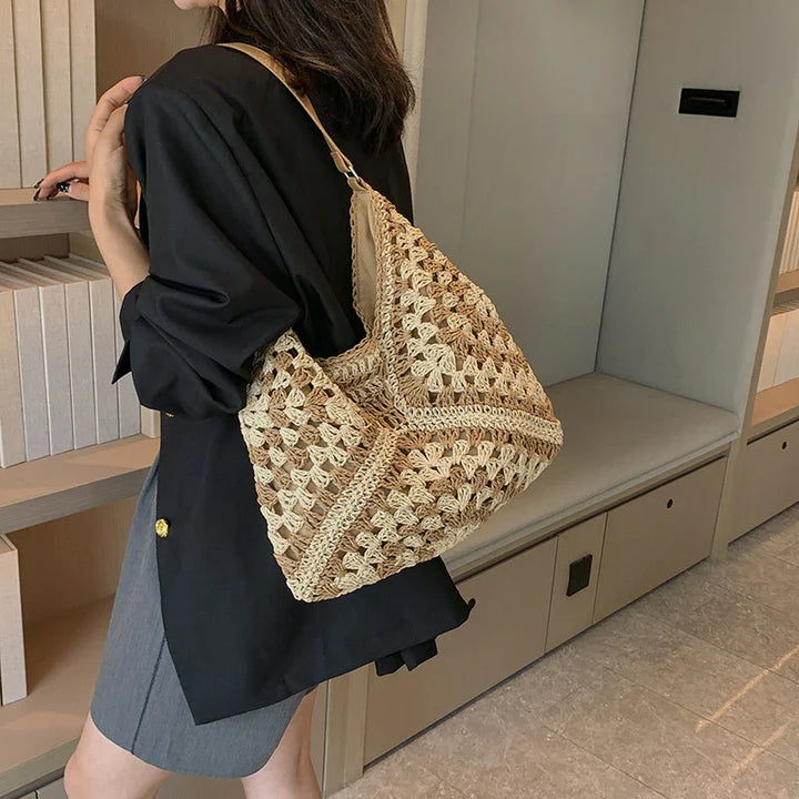 Woman wearing black blazer and gray skirt carrying beige crochet shoulder bag indoors