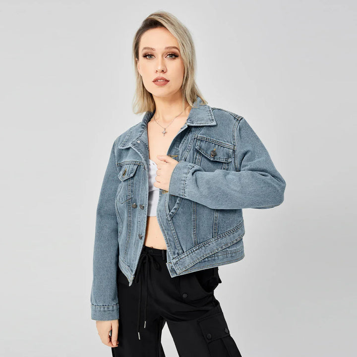 Blonde woman in cropped blue denim jacket and black cargo pants posing against light gray background