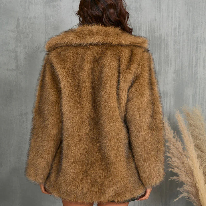 Back view of woman wearing brown faux fur coat against gray wall with dried pampas grass