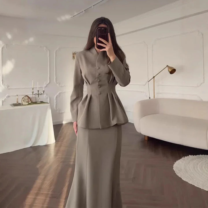 Woman in beige tailored blazer and long skirt taking mirror selfie in elegant room
