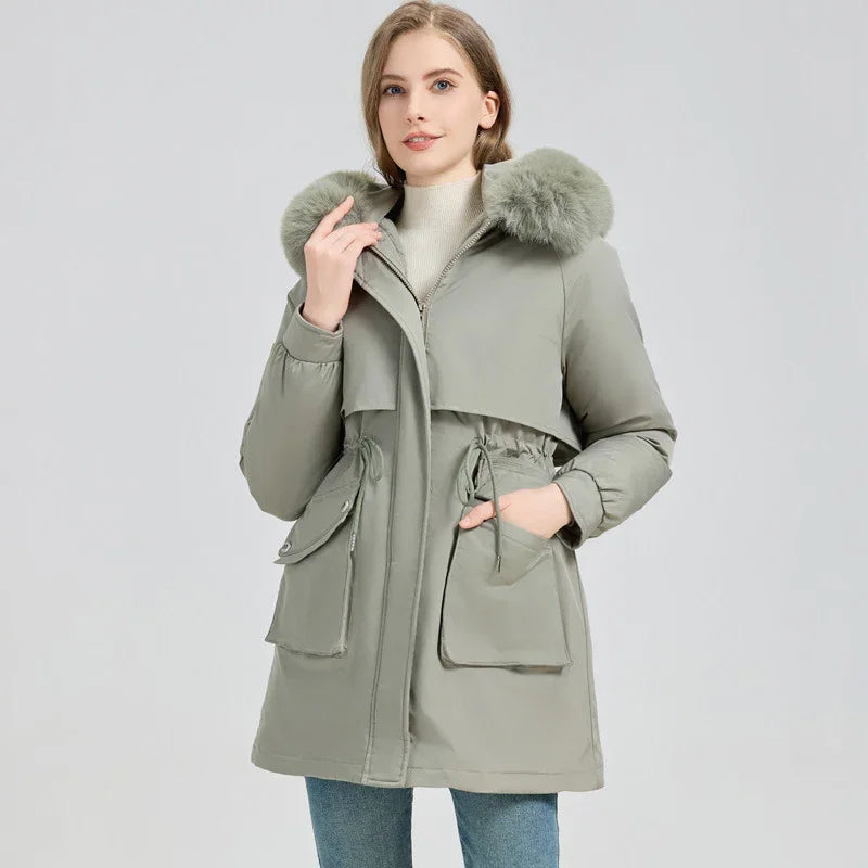 Woman wearing sage green winter parka with fur hood and large front pockets on gray background