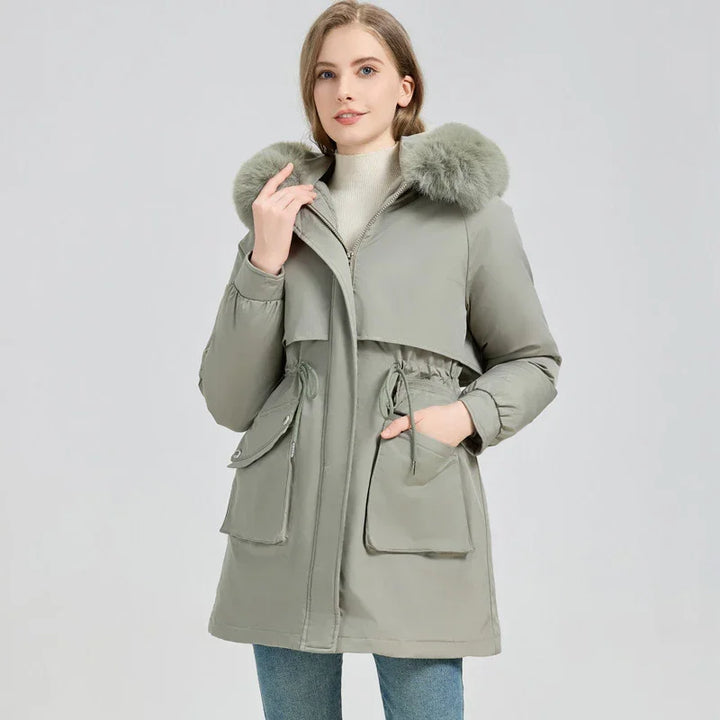 Woman wearing sage green winter parka with fur hood and large front pockets on gray background