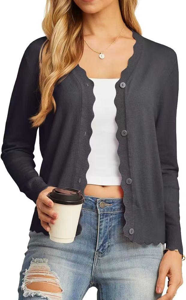 Woman wearing dark gray scalloped cardigan over white crop top and ripped blue jeans holding coffee cup