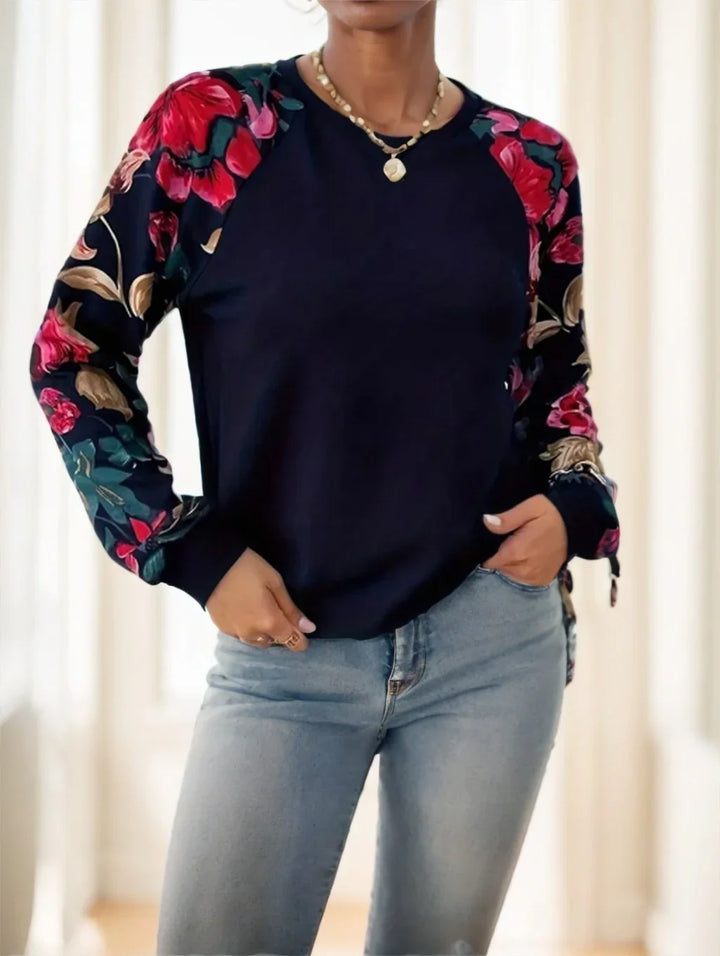 Woman wearing navy blue floral long-sleeve top and light blue jeans in bright indoor setting
