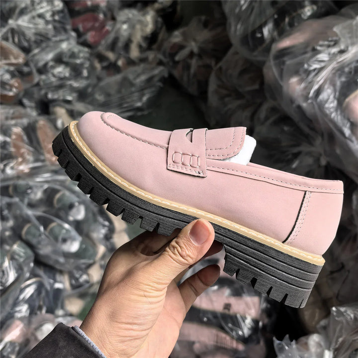 Hand holding pink suede loafer shoe with thick black lug sole and stitched details