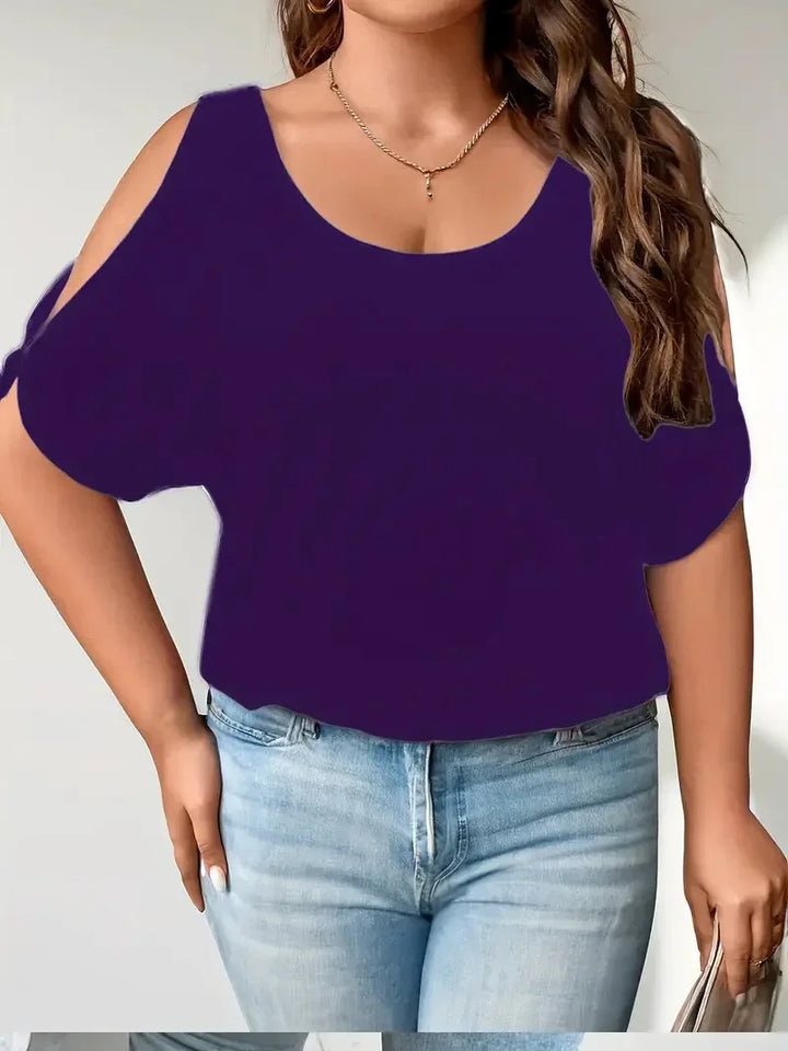 Woman wearing a purple cold shoulder top paired with light blue jeans, accessorized with gold necklace and hoop earrings