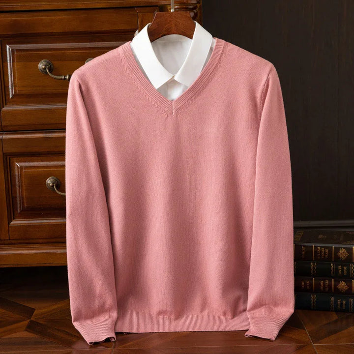 Soft pink V-neck sweater layered over white collared shirt displayed on wooden hanger indoors