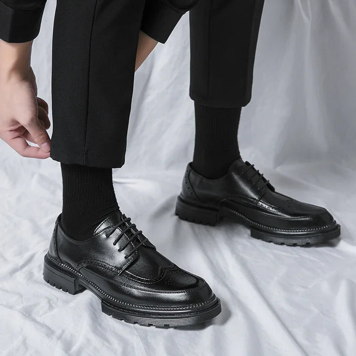 Close-up of black leather dress shoes worn with black socks and pants on a white fabric background