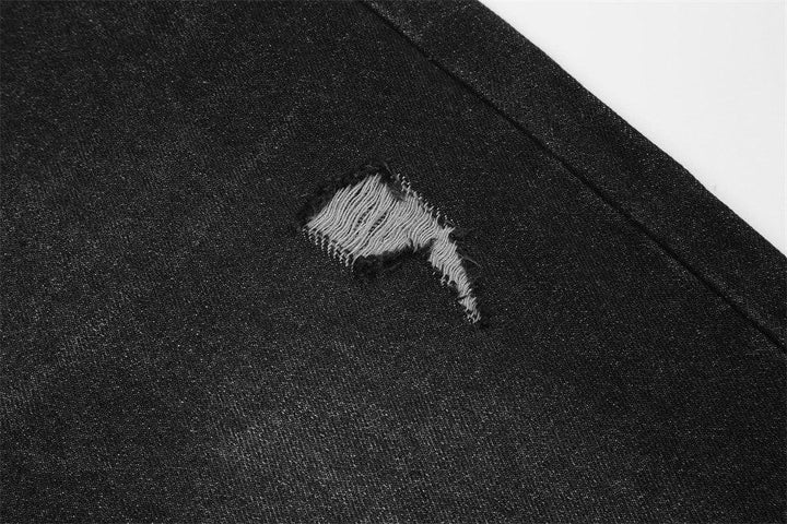 Close-up of black denim fabric with a distressed rip detail near the seam