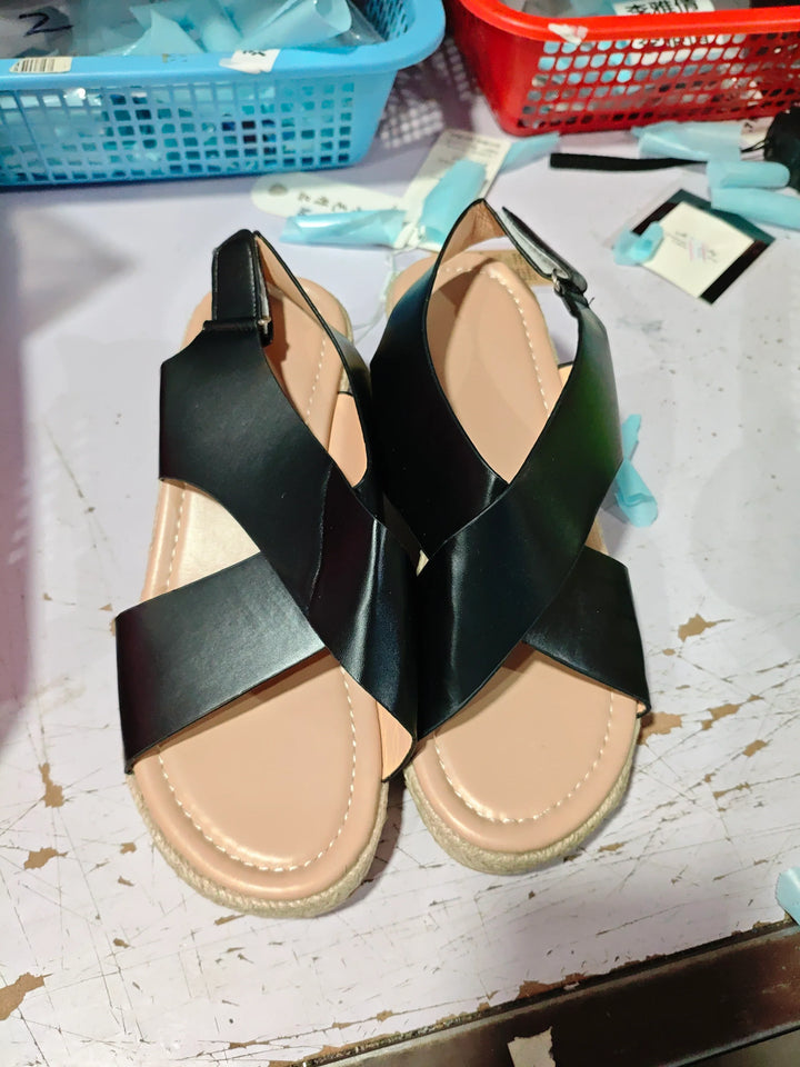 Pair of black leather sandals with beige cushioned insoles on a worn white surface