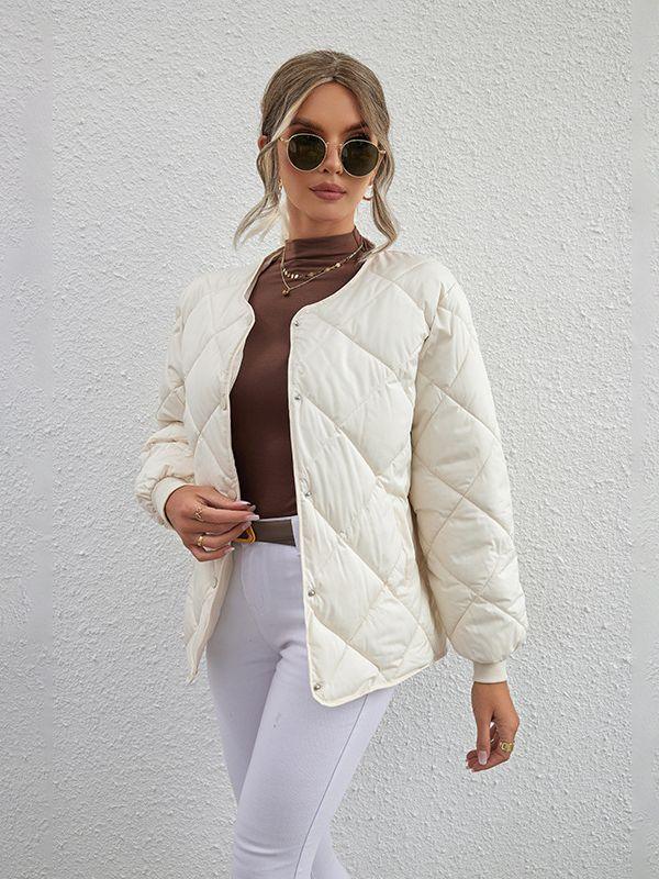 Woman wearing quilted cream jacket, brown turtleneck, white pants, and round sunglasses against textured wall