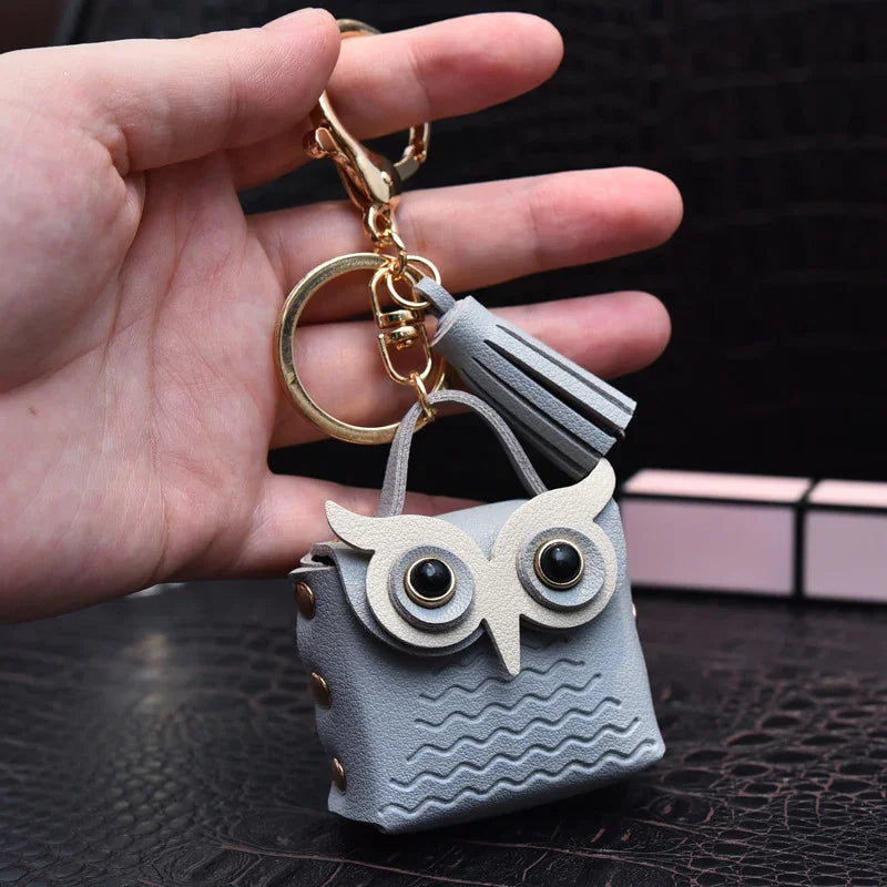 Hand holding a grey leather owl-shaped keychain pouch with gold ring and tassel