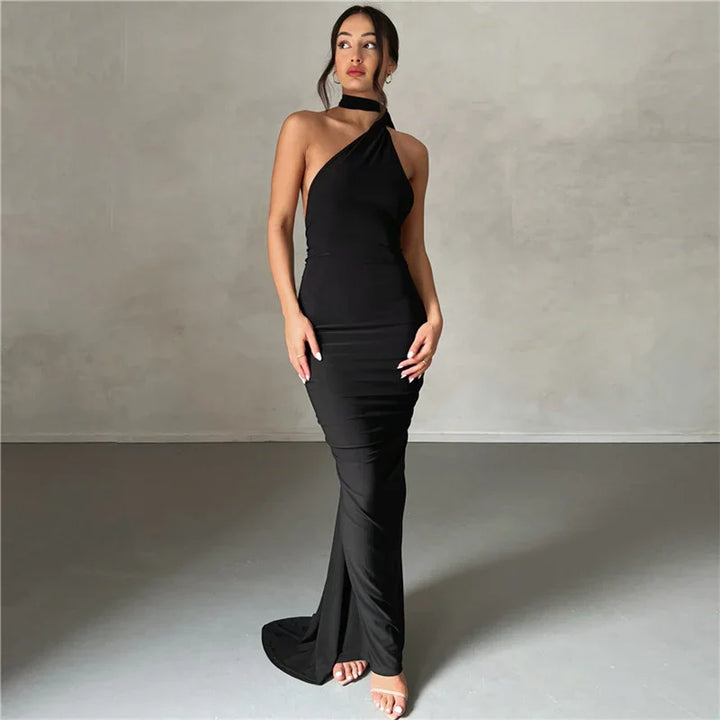Elegant woman wearing a black one-shoulder evening gown with a choker detail, standing in minimalistic studio