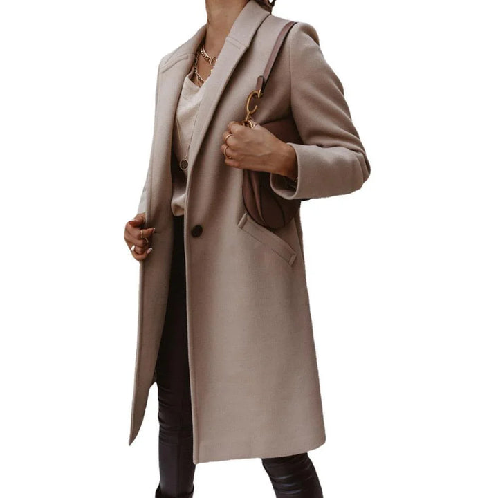Woman wearing a beige wool coat, cream sweater, black pants, and carrying a brown leather shoulder bag