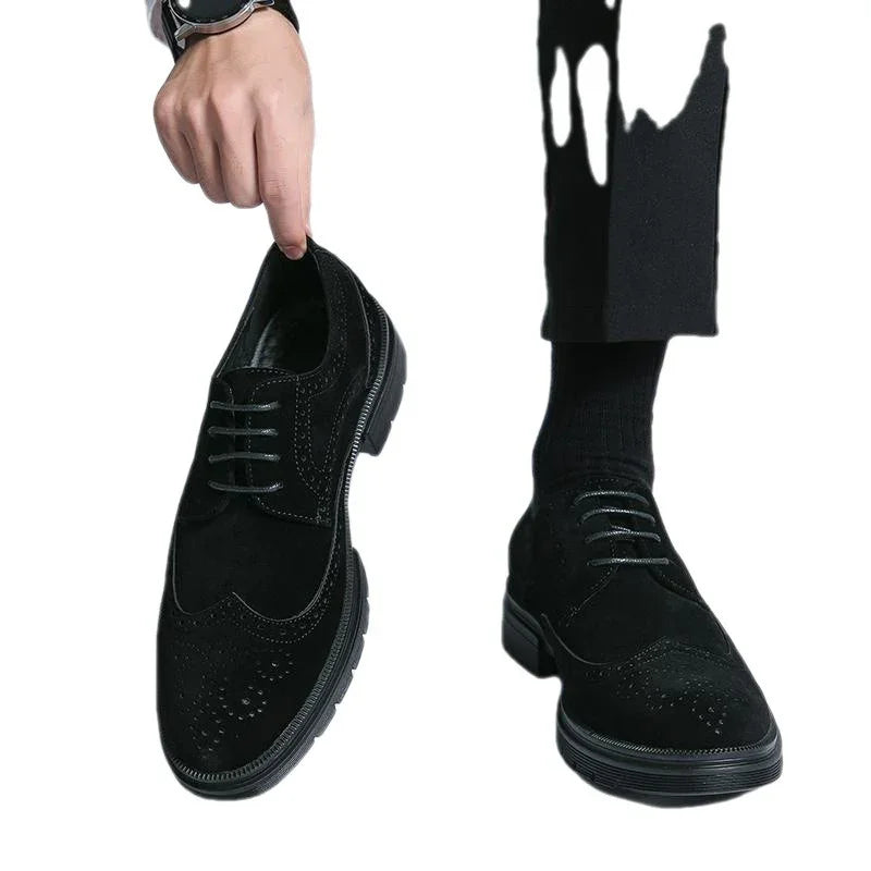 Black suede brogue dress shoes with detailed perforations, one worn with black socks, one held by hand