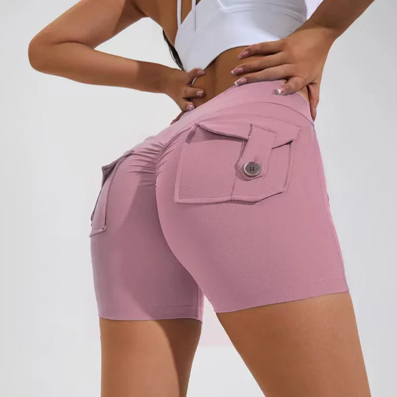 Woman wearing pink ruched booty shorts with flap pockets and button detail in studio