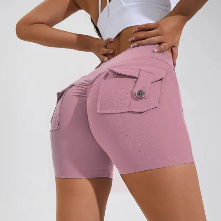 Woman wearing pink ruched booty shorts with flap pockets and button detail in studio