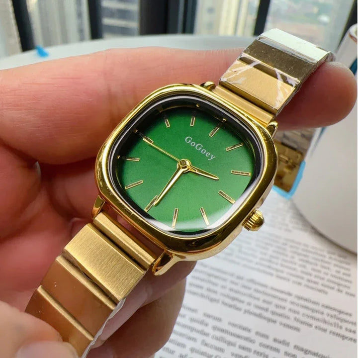 Gold wristwatch with green dial and minimalist design held in hand over paper text background